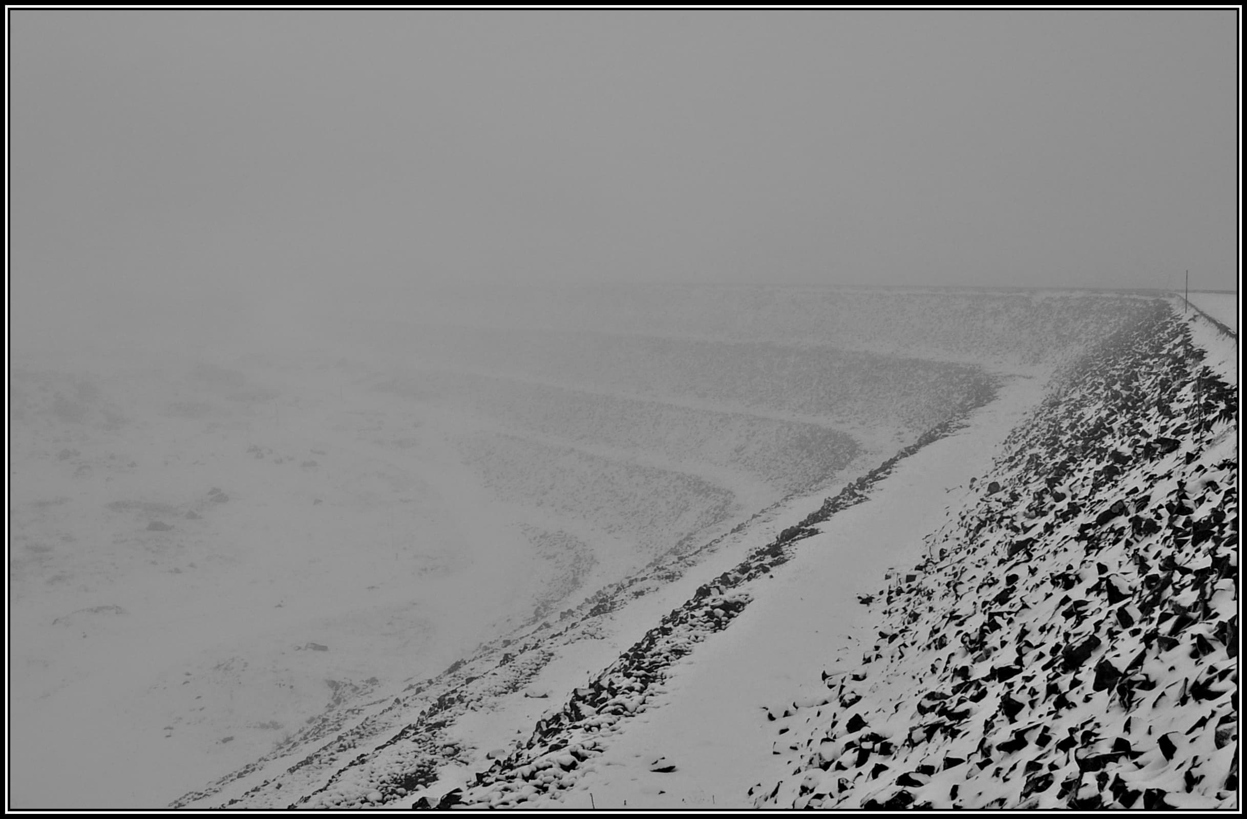Snow and mist closing over the Rocky Valley Storage Dam in the Victorian high country — a pale, near-monochrome winter landscape with the far shore lost in cloud.